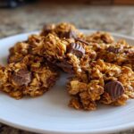Close-up of delicious Peanut Butter Cup Granola clusters on a white plate, featuring oats and chunks of peanut butter cups.