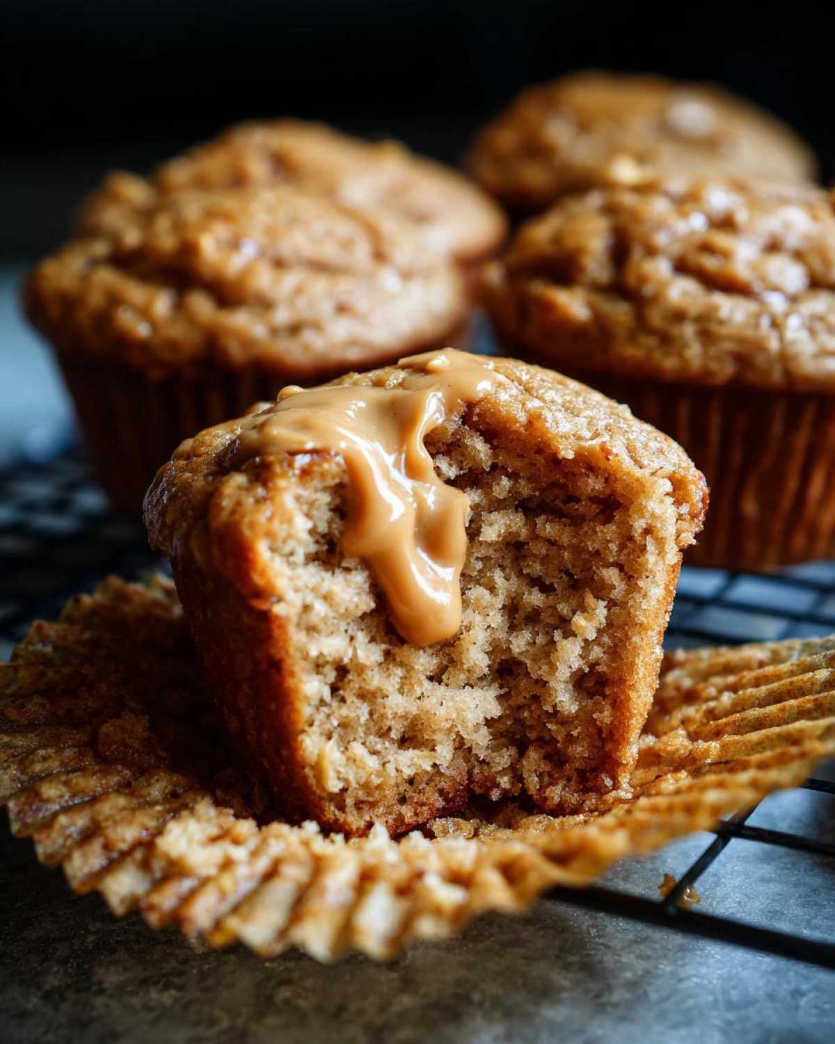 A close-up of a peanut butter protein muffin, broken open to reveal a creamy peanut butter drizzle.