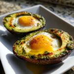 Two halves of avocado baked with eggs and pesto, creating Pesto Eggs in Avocado Boats.