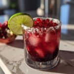 A refreshing Pomegranate Margarita in a salt-rimmed glass, garnished with a lime wheel and fresh pomegranate seeds.