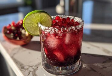 A refreshing Pomegranate Margarita in a salt-rimmed glass, garnished with a lime wheel and fresh pomegranate seeds.