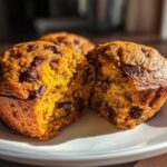 A close-up view of a broken Pumpkin Chocolate Chip Muffin, revealing its moist interior and chocolate chips.