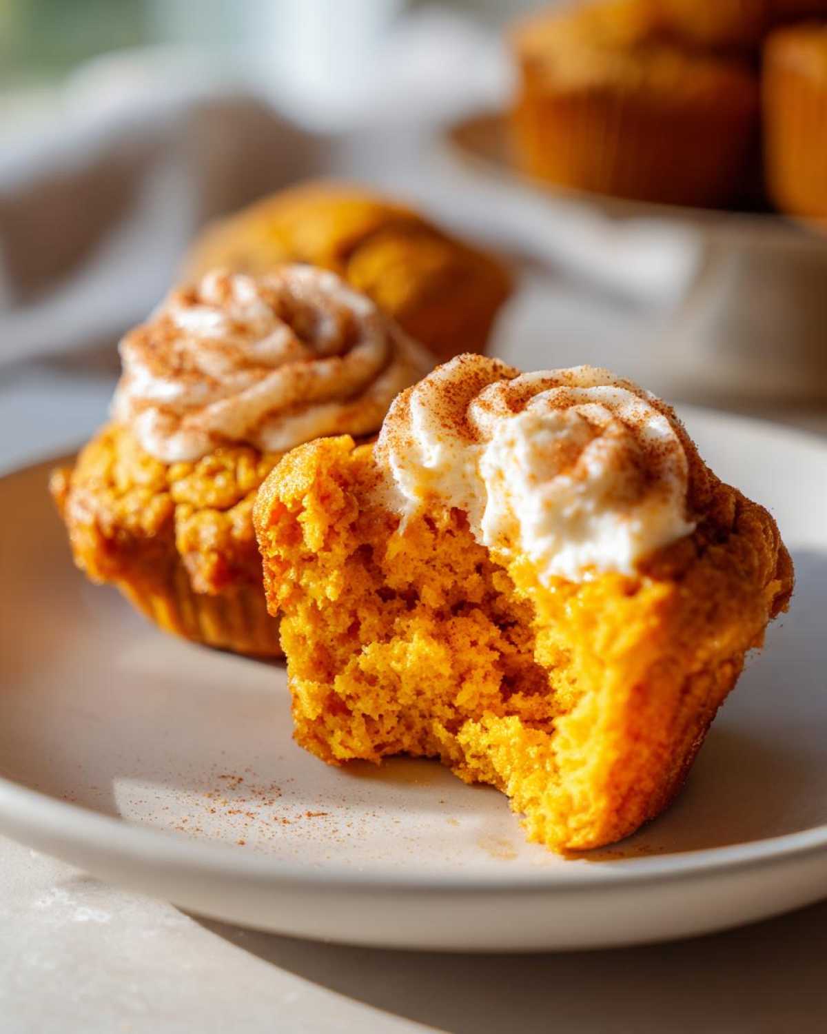 Close-up of a bitten Pumpkin Cream Cheese Muffin topped with cream cheese frosting and cinnamon.