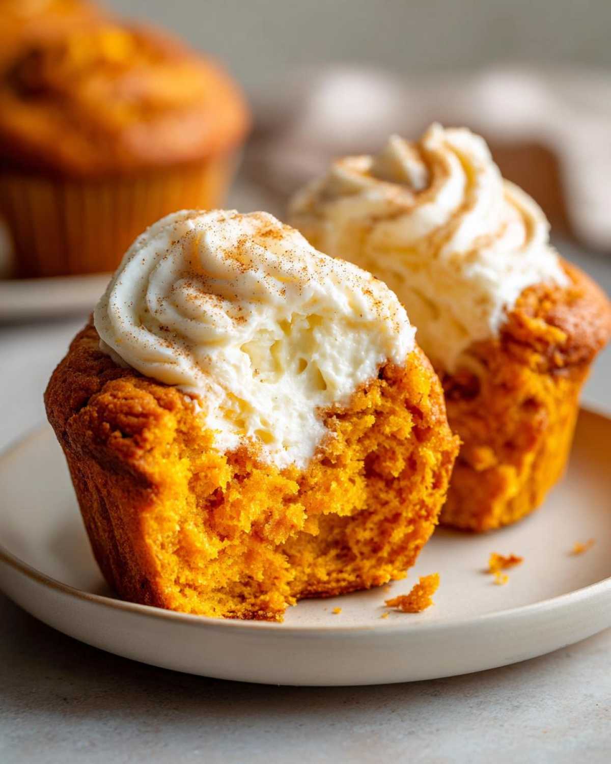 A close-up of a Pumpkin Cream Cheese Muffin, cut in half to reveal a creamy center and topped with swirls of cream cheese frosting and cinnamon.