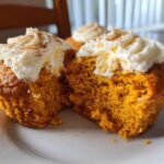 Close-up of two Pumpkin Cream Cheese Muffins, one split open, topped with creamy frosting and cinnamon.