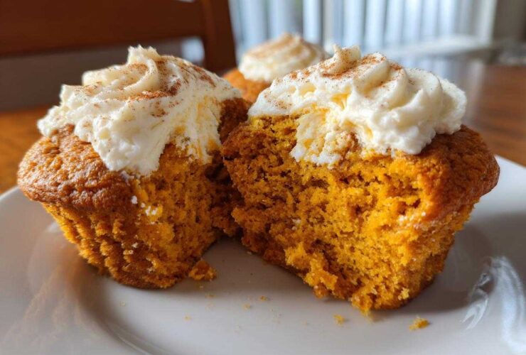 Close-up of two Pumpkin Cream Cheese Muffins, one split open, topped with creamy frosting and cinnamon.