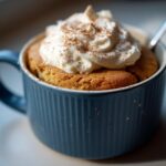 A close-up of a delicious Pumpkin Spice Latte Mug Cake topped with whipped cream and cinnamon.
