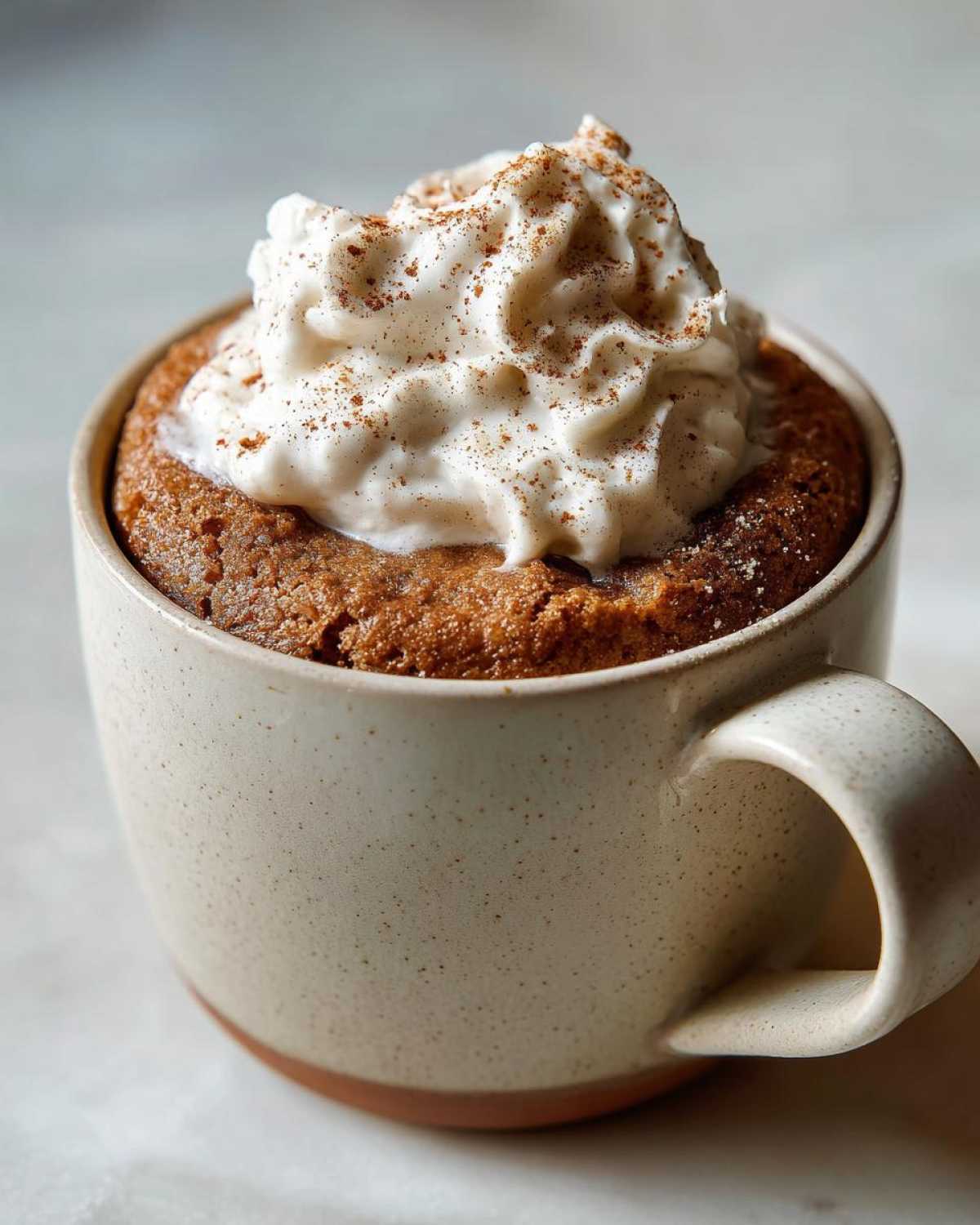 A close-up of a delicious Pumpkin Spice Latte Mug Cake topped with whipped cream and a sprinkle of cinnamon.