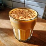 A close-up of a creamy Pumpkin Spice Protein Smoothie topped with cinnamon powder in a glass.
