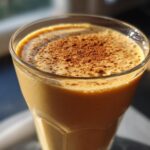A close-up of a creamy Pumpkin Spice Protein Smoothie topped with a sprinkle of cinnamon.