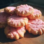 A close-up of a stack of pink Raspberry Rosewater Shortbread cookies on a wooden surface.