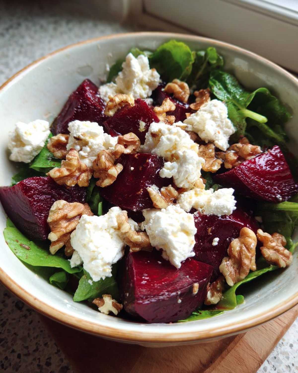 A close-up of a vibrant Roasted Beet & Goat Cheese Salad with fresh greens, crumbled goat cheese, and walnuts.