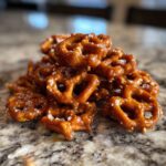 A close-up of a pile of glistening salted caramel pretzel bites, sprinkled with coarse sea salt.