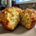 A split Savory Zucchini Cheese Muffin showing the fluffy interior with shredded zucchini and cheese.