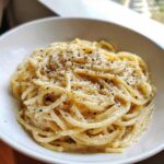 A close-up of creamy Spaghetti Cacio e Pepe topped with grated cheese and black pepper.