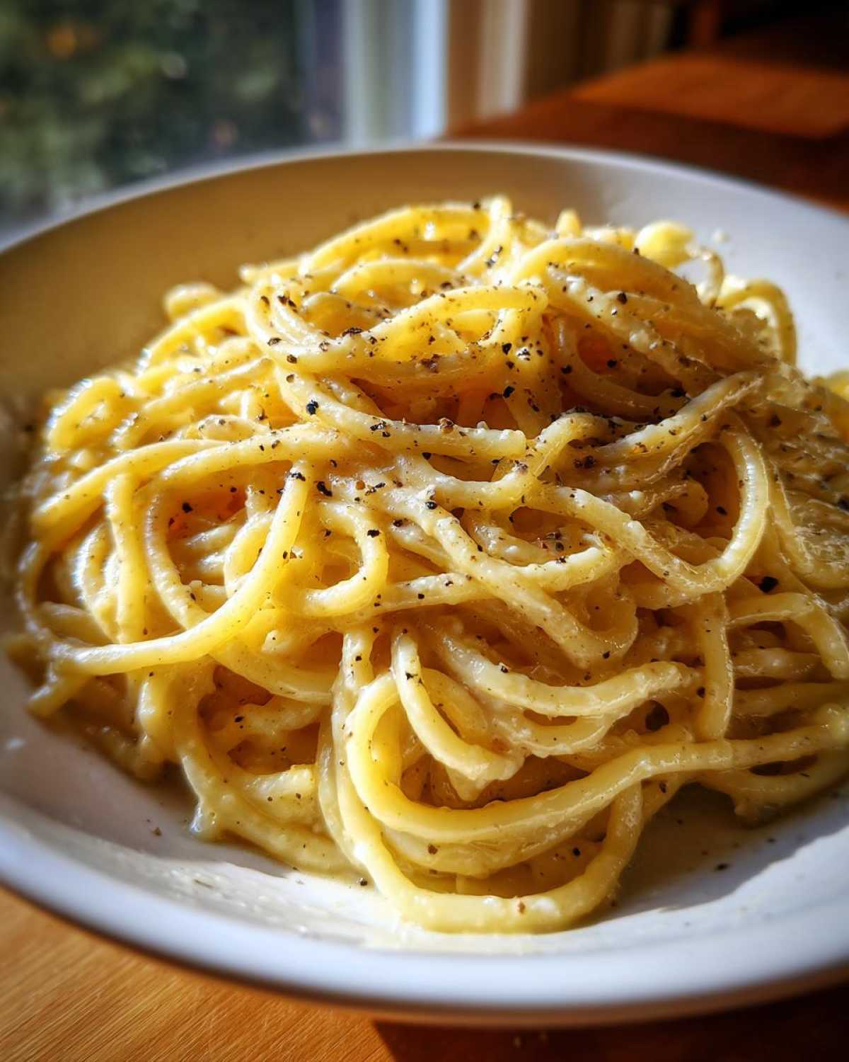 A close-up of creamy Spaghetti Cacio e Pepe, coated in cheese and generously sprinkled with black pepper.