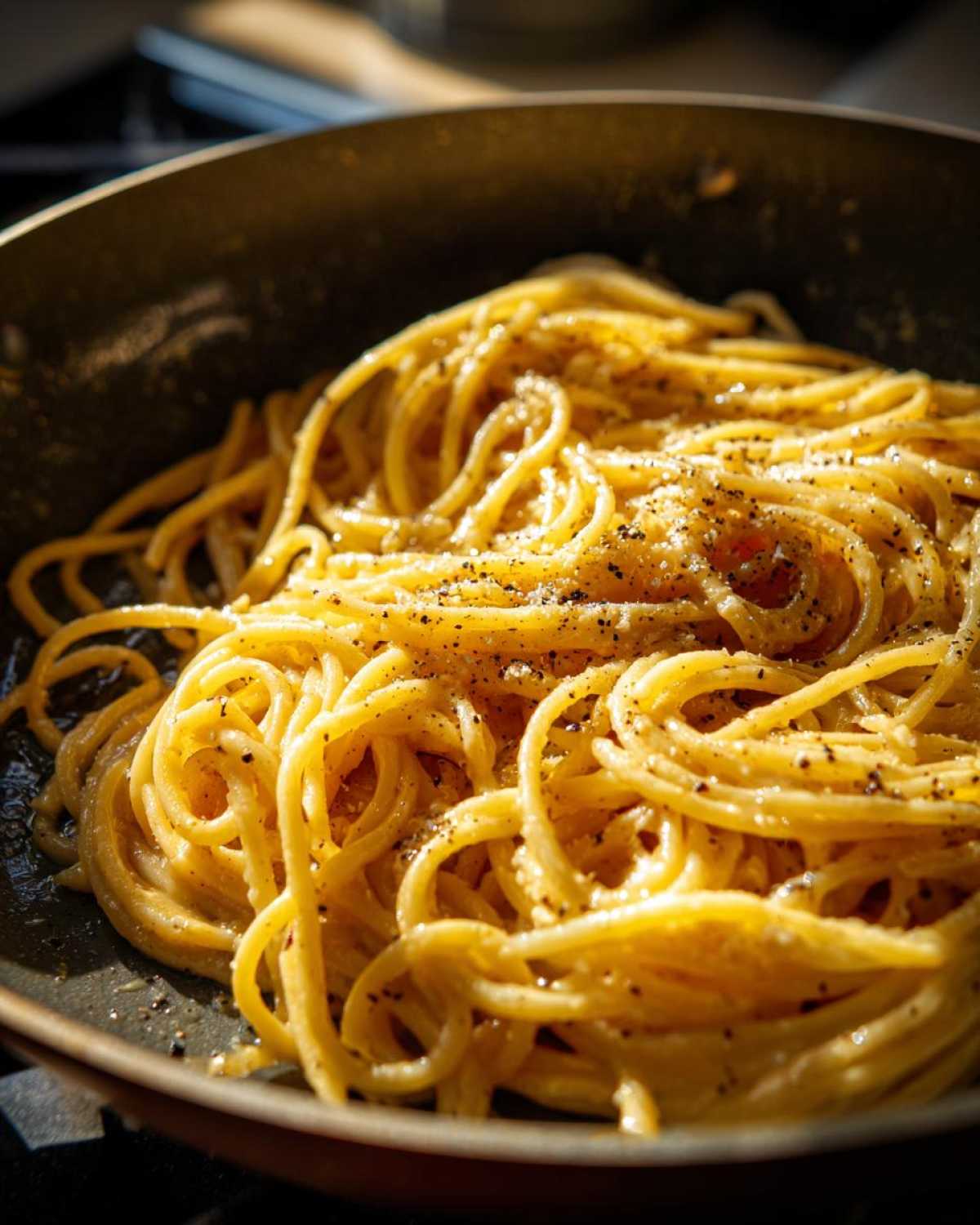Close-up of creamy Spaghetti Cacio e Pepe being tossed in a pan, with cracked black pepper.