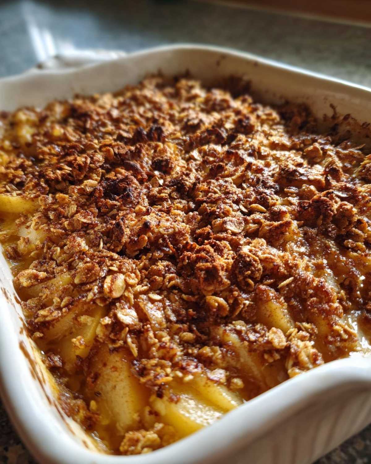 Close-up of a Spiced Pear Crisp in a white baking dish, showing baked pear slices and a golden-brown oat topping.