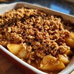 Close-up of a freshly baked Spiced Pear Crisp in a white and red baking dish, showing tender pears and a golden crumble topping.