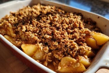 Close-up of a freshly baked Spiced Pear Crisp in a white and red baking dish, showing tender pears and a golden crumble topping.