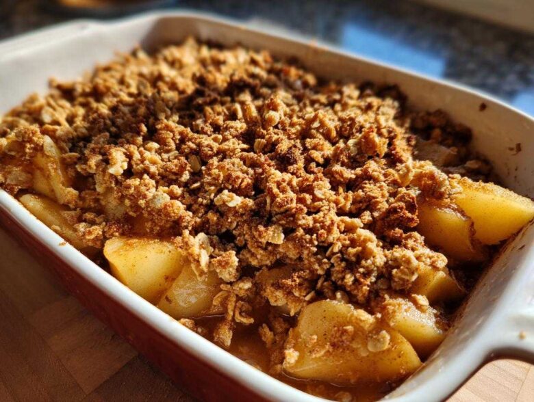Close-up of a freshly baked Spiced Pear Crisp in a white and red baking dish, showing tender pears and a golden crumble topping.