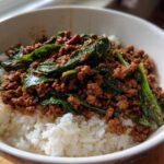 A close-up of Spicy Thai Basil Beef (Pad Kra Pao) served over fluffy white rice in a white bowl.