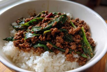 A close-up of Spicy Thai Basil Beef (Pad Kra Pao) served over fluffy white rice in a white bowl.