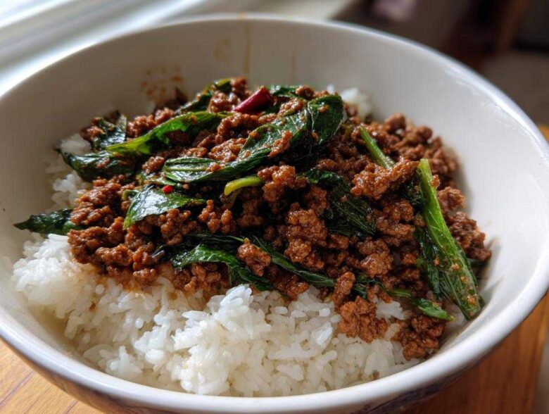 A close-up of Spicy Thai Basil Beef (Pad Kra Pao) served over fluffy white rice in a white bowl.