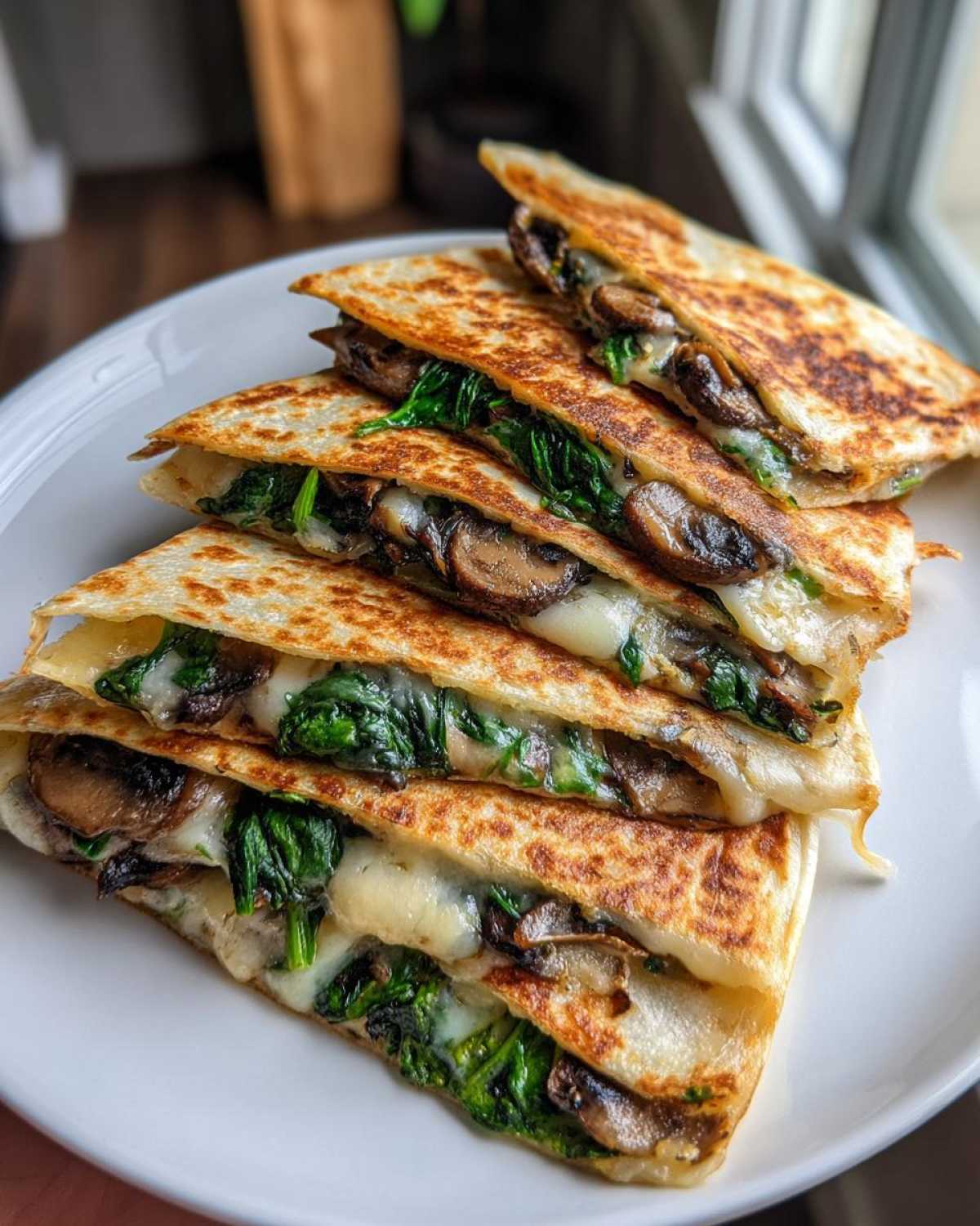 A stack of golden-brown Spinach Mushroom Quesadilla slices filled with melted cheese, spinach, and mushrooms.