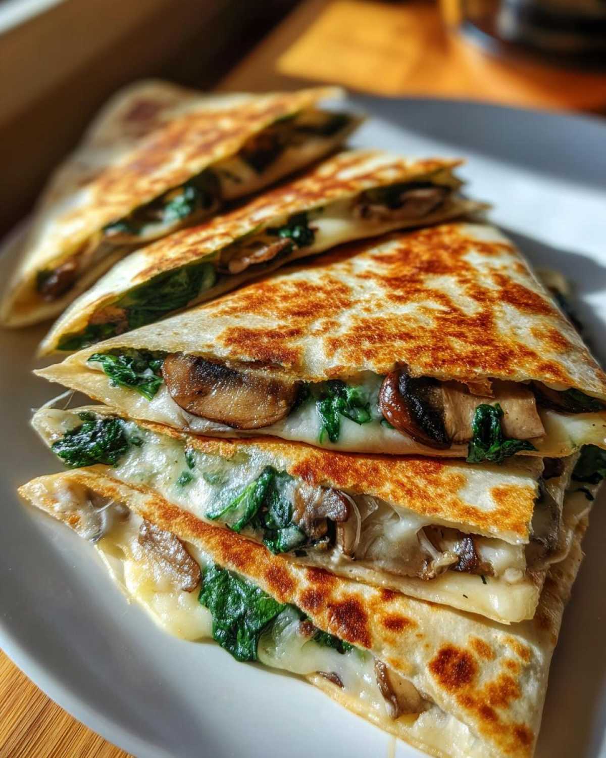 Close-up of golden-brown Spinach Mushroom Quesadilla slices stacked on a white plate, showing melted cheese and filling.