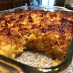 A close-up of a golden-brown, baked Squash Casserole in a glass dish, with a serving removed.