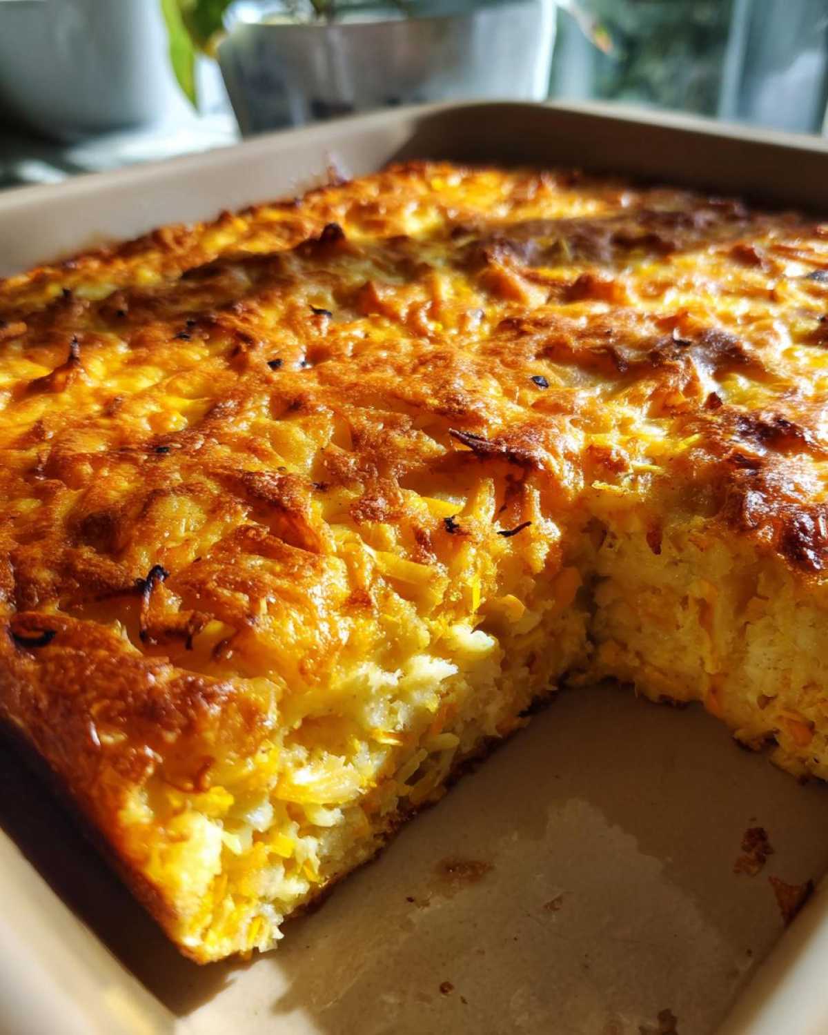 Close-up of a golden brown, baked Squash Casserole in a tan baking dish, with a slice removed.