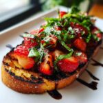 A slice of toasted bread topped with fresh strawberries, basil, and balsamic glaze for Strawberry Balsamic Bruschetta.