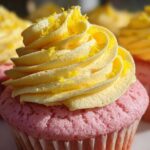 Close-up of a pink Strawberry Lemonade Cupcake topped with swirled yellow lemon frosting and lemon zest.