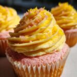 Close-up of three Strawberry Lemonade Cupcakes with swirled yellow frosting and pink and yellow sprinkles.