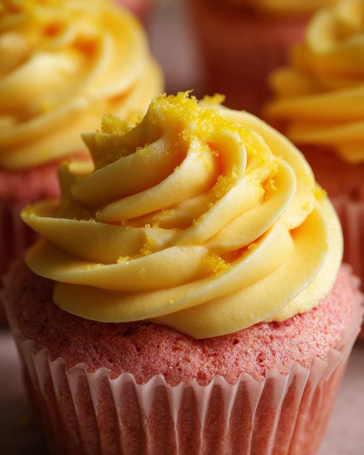 Close-up of a pink Strawberry Lemonade Cupcake topped with swirled yellow frosting and yellow zest.