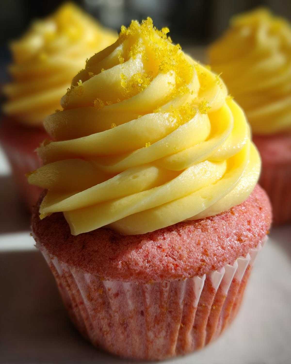 Close-up of a pink Strawberry Lemonade Cupcake topped with swirled yellow frosting and yellow sugar crystals.