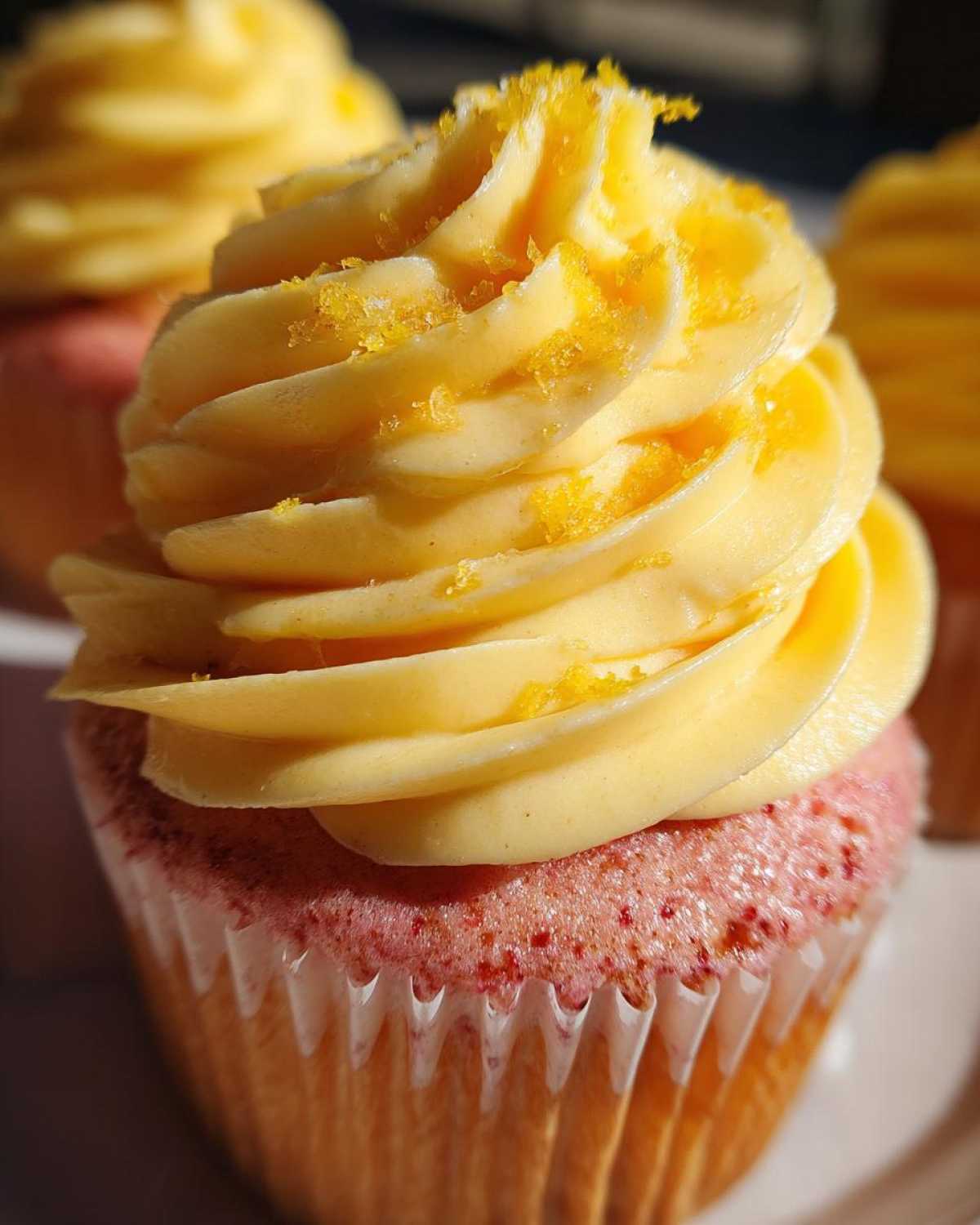 Close-up of a Strawberry Lemonade Cupcake with swirled yellow frosting and orange zest.