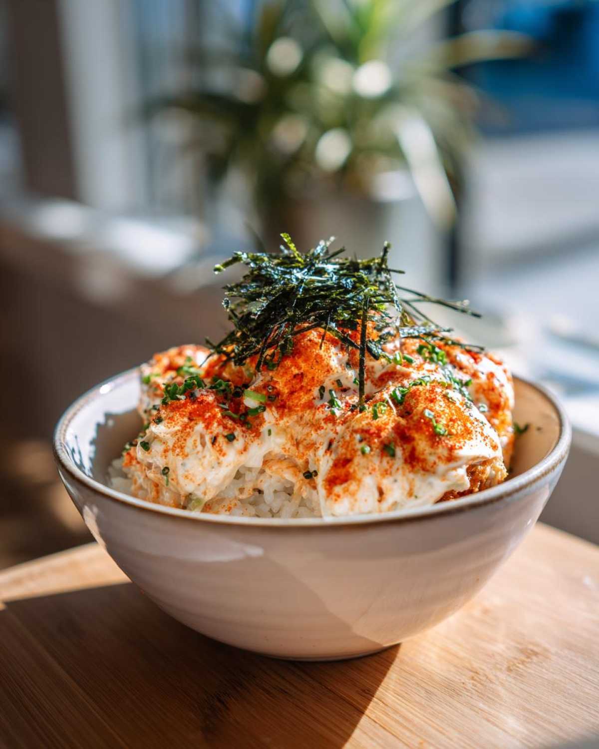 A close-up of a bowl of Sushi Bake, featuring rice topped with creamy sauce, furikake, and nori.
