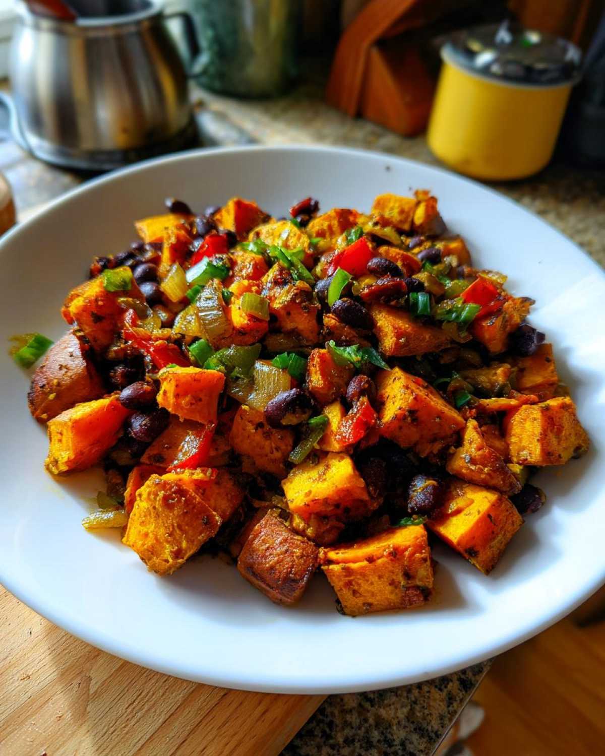 A white bowl filled with a colorful Sweet Potato & Black Bean Hash, featuring roasted sweet potato cubes, black beans, and diced bell peppers.