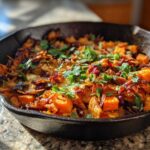 A close-up of a cast iron skillet filled with a colorful Sweet Potato & Black Bean Hash, garnished with fresh cilantro.