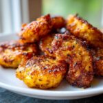 A close-up shot of golden-brown, crispy Sweet Potato Tater Tots piled on a white plate, seasoned with herbs.