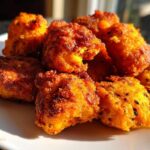 A close-up of golden-brown, crispy Sweet Potato Tater Tots piled on a white plate, ready to be eaten.