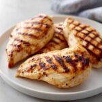 Four perfectly grilled chicken breasts with char marks, served on a white plate, showcasing the delicious Sweet Tea Brine Chicken.