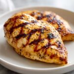 Two juicy grilled chicken breasts seasoned with herbs, showcasing beautiful grill marks from cooking.