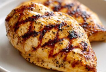 Two juicy grilled chicken breasts seasoned with herbs, showcasing beautiful grill marks from cooking.