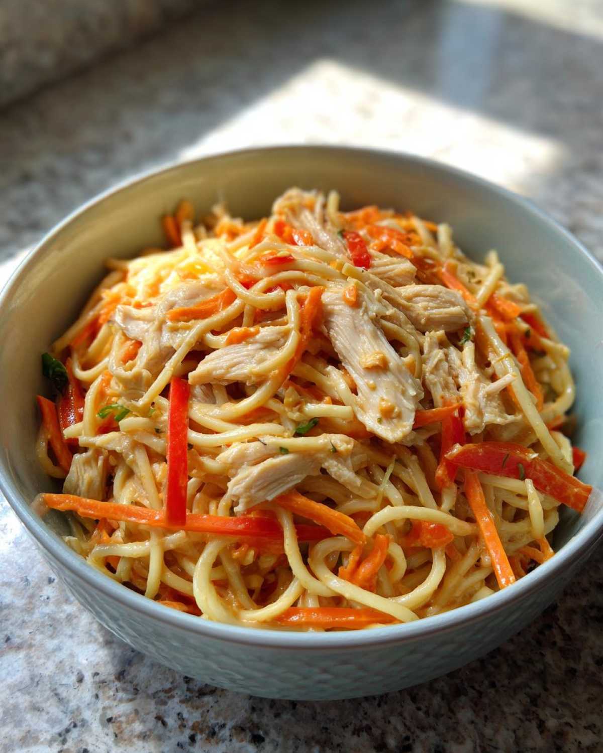 A close-up of a bowl filled with Thai Peanut Chicken Noodle Salad, featuring noodles, shredded chicken, and julienned carrots.