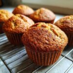 A close-up shot of freshly baked vegan banana muffins cooling on a wire rack.