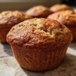 Close-up of a golden-brown vegan banana muffin with a slightly cracked top, showcasing its texture.