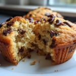 Close-up of a delicious vegan chocolate chip muffin, broken in half to reveal a fluffy interior dotted with chocolate chips.
